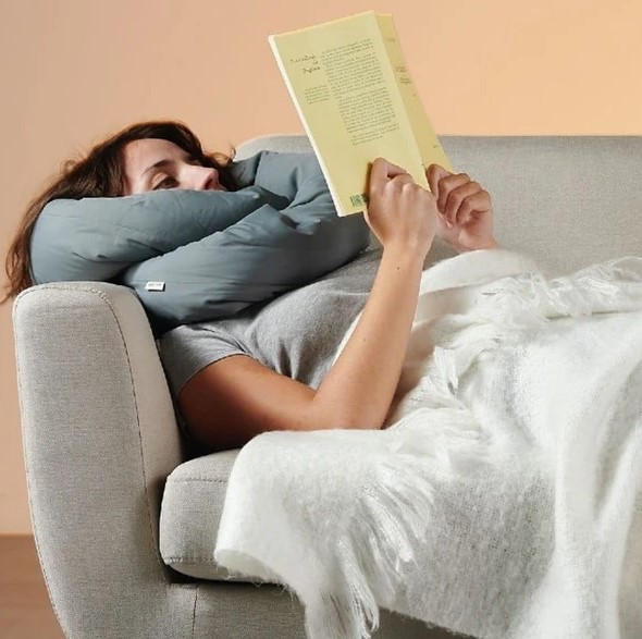 Person relaxing on a couch reading a book with the infinity pillow supporting the neck