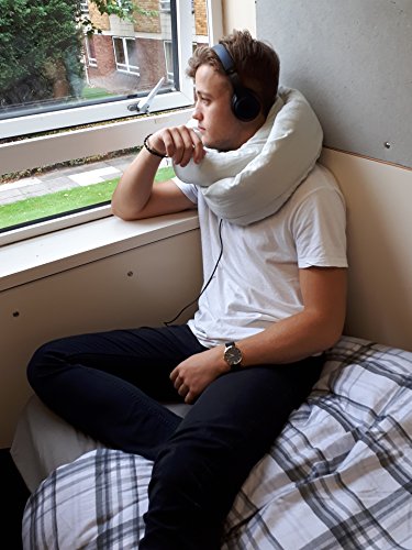 Traveler resting against a window with the infinity pillow wrapped around the neck while listening to headphones